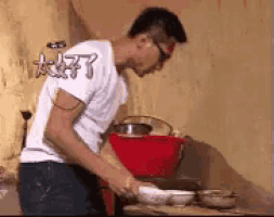 a man in a white shirt is cooking in a kitchen with a red bowl .