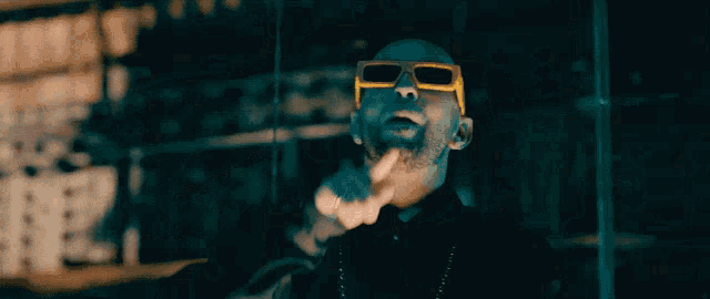 a man wearing a black jacket and yellow sunglasses is pointing