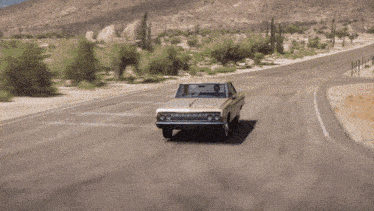 a white car is driving down a desert road with mountains in the background