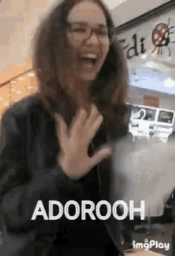 a woman wearing glasses and a black jacket is laughing and waving her hands in a mall .