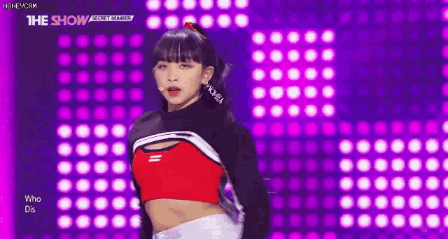 a woman in a red and black crop top is dancing on a stage with purple lights behind her .