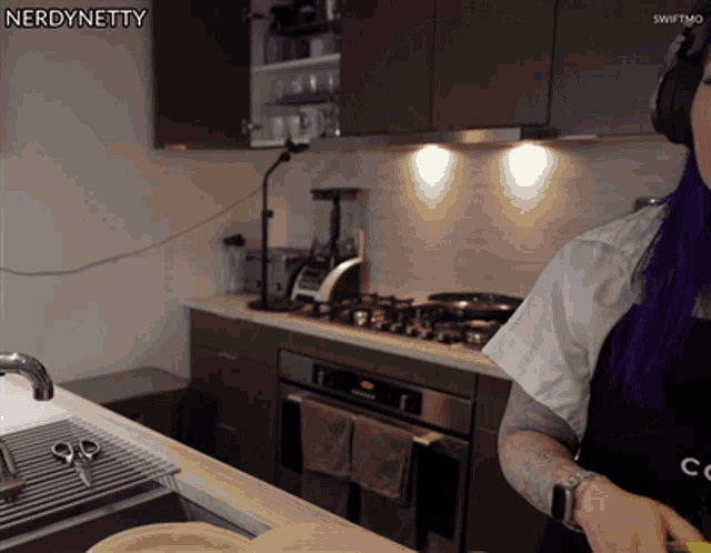 a woman with purple hair is cooking in a kitchen with nerdynetty written on the corner