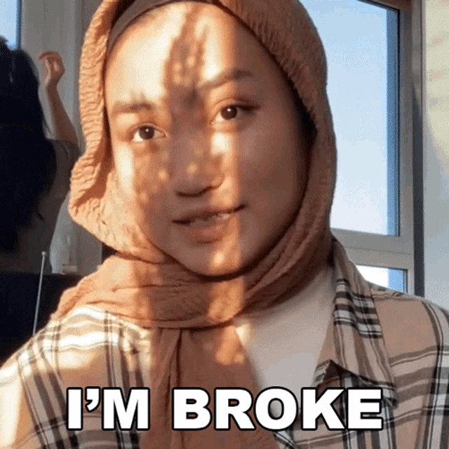 a woman wearing a hijab says i 'm broke in front of a window