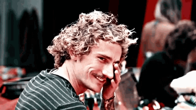 a man with curly hair and a mustache is smiling and talking on a cell phone