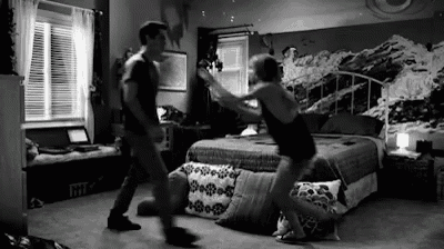 a man and woman are dancing in a bedroom in front of a bed .
