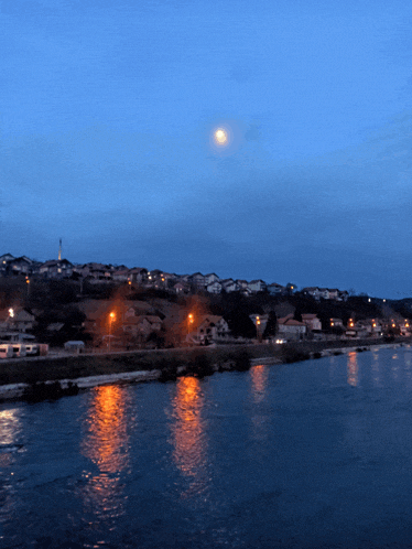 a full moon is visible over a river with a residential area in the background
