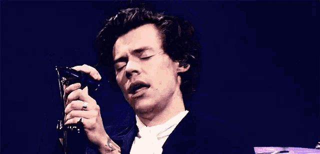 harry styles is smiling while singing into a microphone on a stage .