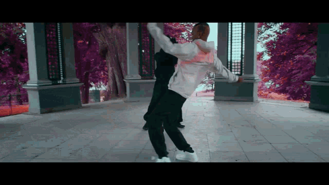 a man in a black and white jacket is dancing in front of purple trees