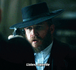 a man with a beard is wearing a black hat and talking to another man