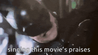 a man in a batman costume is singing a song that says singing this movie 's praises