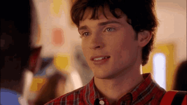 a young man in a plaid shirt is smiling and looking at something