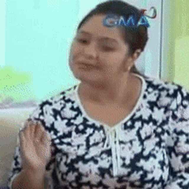 a woman in a floral shirt is sitting on a couch with a gma logo on her head .