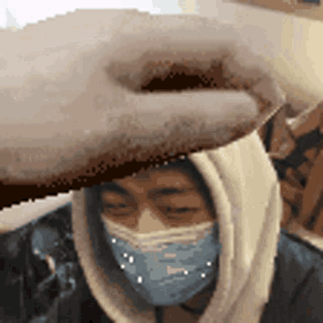 a person wearing a face mask and a hoodie is being touched by a hand .