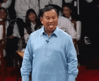 a man in a blue shirt is sticking his tongue out while standing in front of a crowd of people .