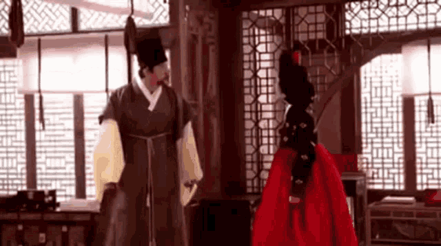a man and a woman in traditional korean clothing are standing in a room .
