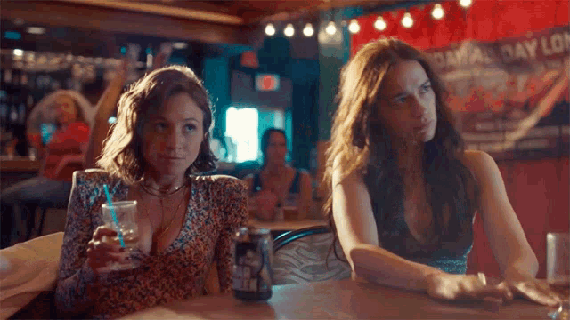 two women sitting at a table with a can of beer
