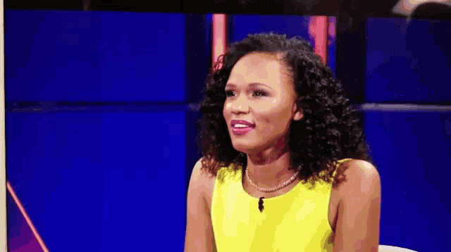 a woman in a yellow top is sitting in front of a blue background