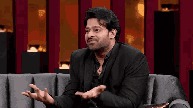a man in a suit is sitting on a couch with his hands out