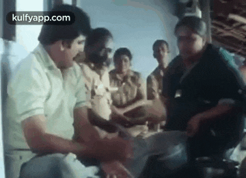 a group of people are standing around a table and talking to each other in a room .