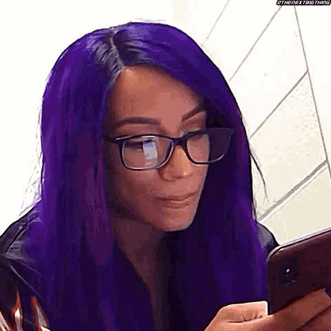 a woman with purple hair and glasses is using a cell phone .