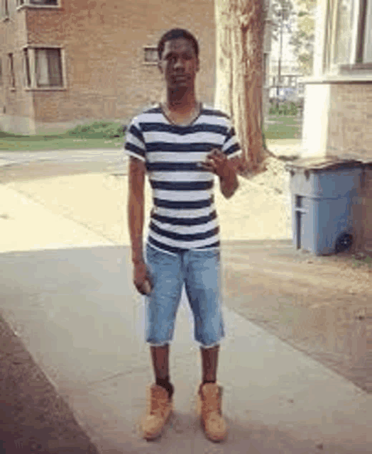 a man wearing a striped shirt and shorts is standing on a sidewalk .