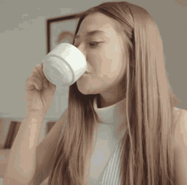a woman with long hair drinking from a white mug