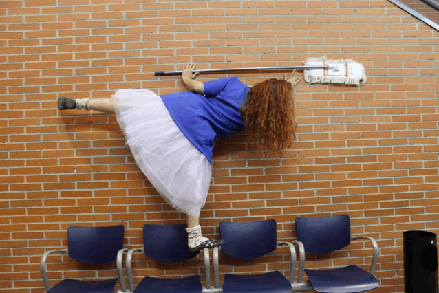 a woman in a blue shirt and white skirt is leaning against a brick wall with a mop on her head