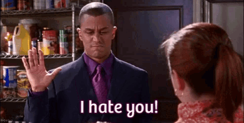 a man in a suit and tie is giving the middle finger to a woman in a kitchen .