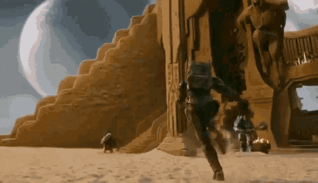 a man is walking in the sand in front of a pyramid .
