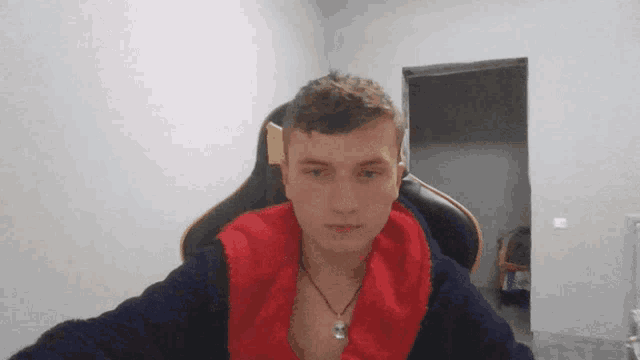 a young man is sitting in a chair with a red and blue jacket on