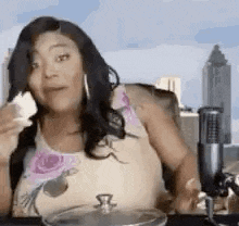 a woman is sitting at a table in front of a microphone eating a piece of cake .