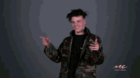 a young man in a camo jacket is giving a thumbs up sign .