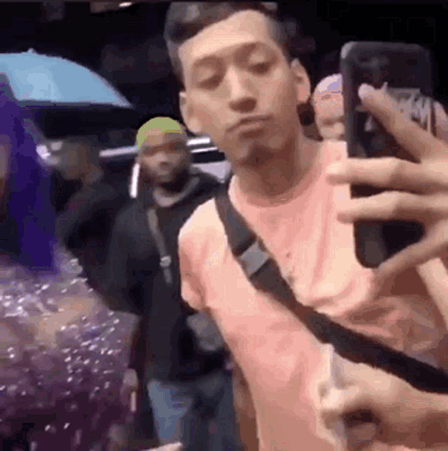 a man in a pink shirt is taking a selfie with his phone .