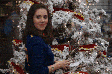 a woman is decorating a christmas tree with red and yellow ribbons