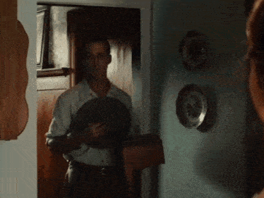 a man is standing in a doorway holding a hat while a woman looks on