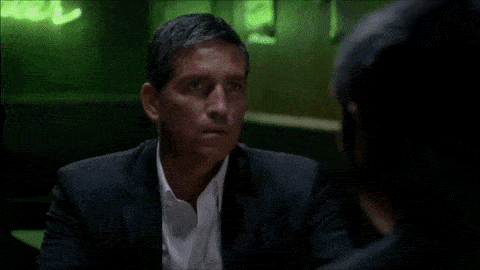 an older man sits at a bar with bottles of alcohol behind him