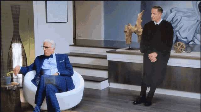 a man in a suit sits in a chair next to another man