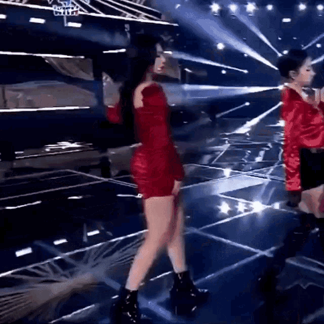 a woman in a red dress is dancing on a stage with other people .