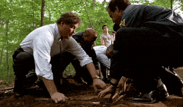 a group of men are kneeling down in the dirt and one of them is wearing a blue jacket with the number 21 on it