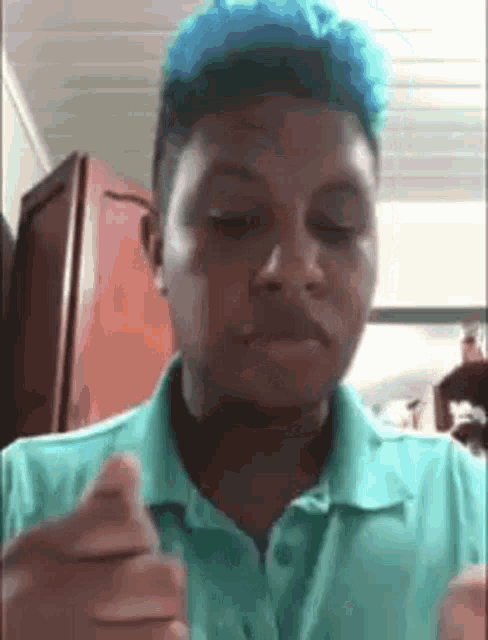a young man with blue hair is making a funny face while wearing a blue shirt .