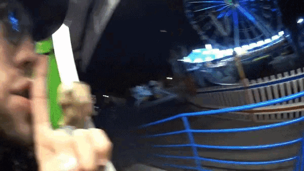a person is holding a green object in front of a blue ferris wheel