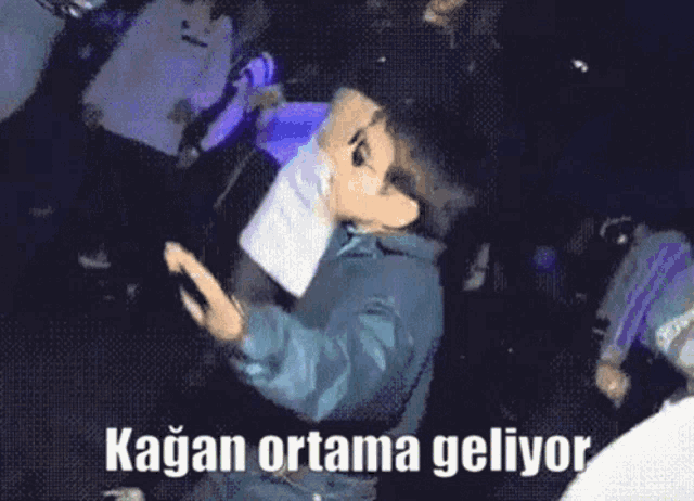 a man with a tattoo on his face is dancing in a club with the words kagan ortama geliyor written below him .