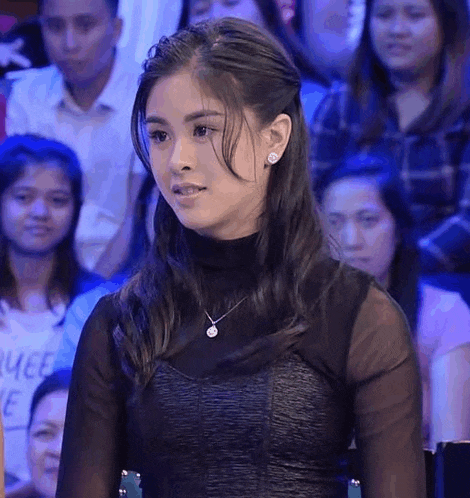 a woman is sitting in front of a crowd of people wearing a black top and a necklace .