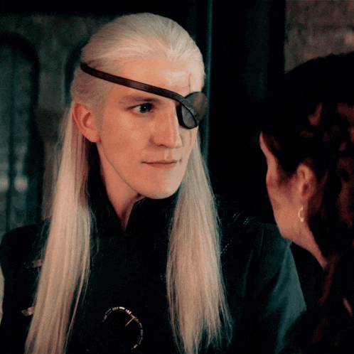 a man with long white hair and an eye patch on his forehead looks at a woman