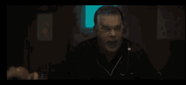 a man with a ring on his finger is sitting in a dark room talking to another man