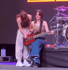 a woman is playing a bass guitar while another woman looks on