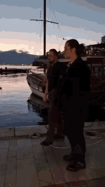 two men standing on a dock looking at a boat