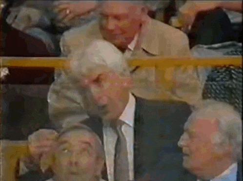a man in a suit and tie is talking to another man in a crowd