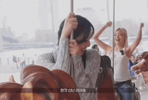 a woman is riding a merry go round with another woman standing behind her .