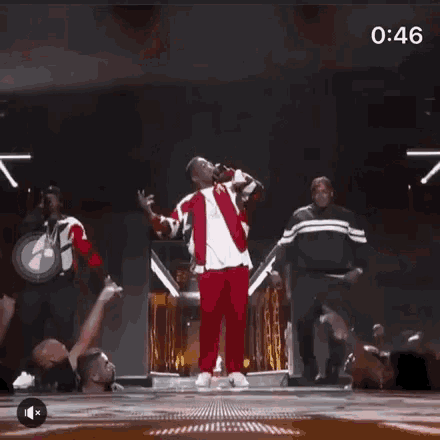 a man is standing on a stage holding a microphone while a group of people are dancing around him .